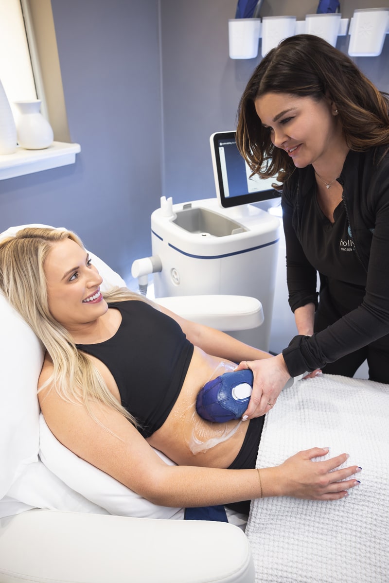 Woman happily lays on bed as a medspa specialist places a coolsculpting tool on her belly. Call us for more information on body contouring treatments in Kansas City with our trusted team.