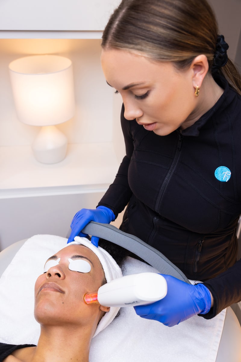 Woman holds laser resurfx tool to another woman’s cheek as she lays calmly. Contact us for an experienced KC med spa professional for laser hair and skin rejuvenation.